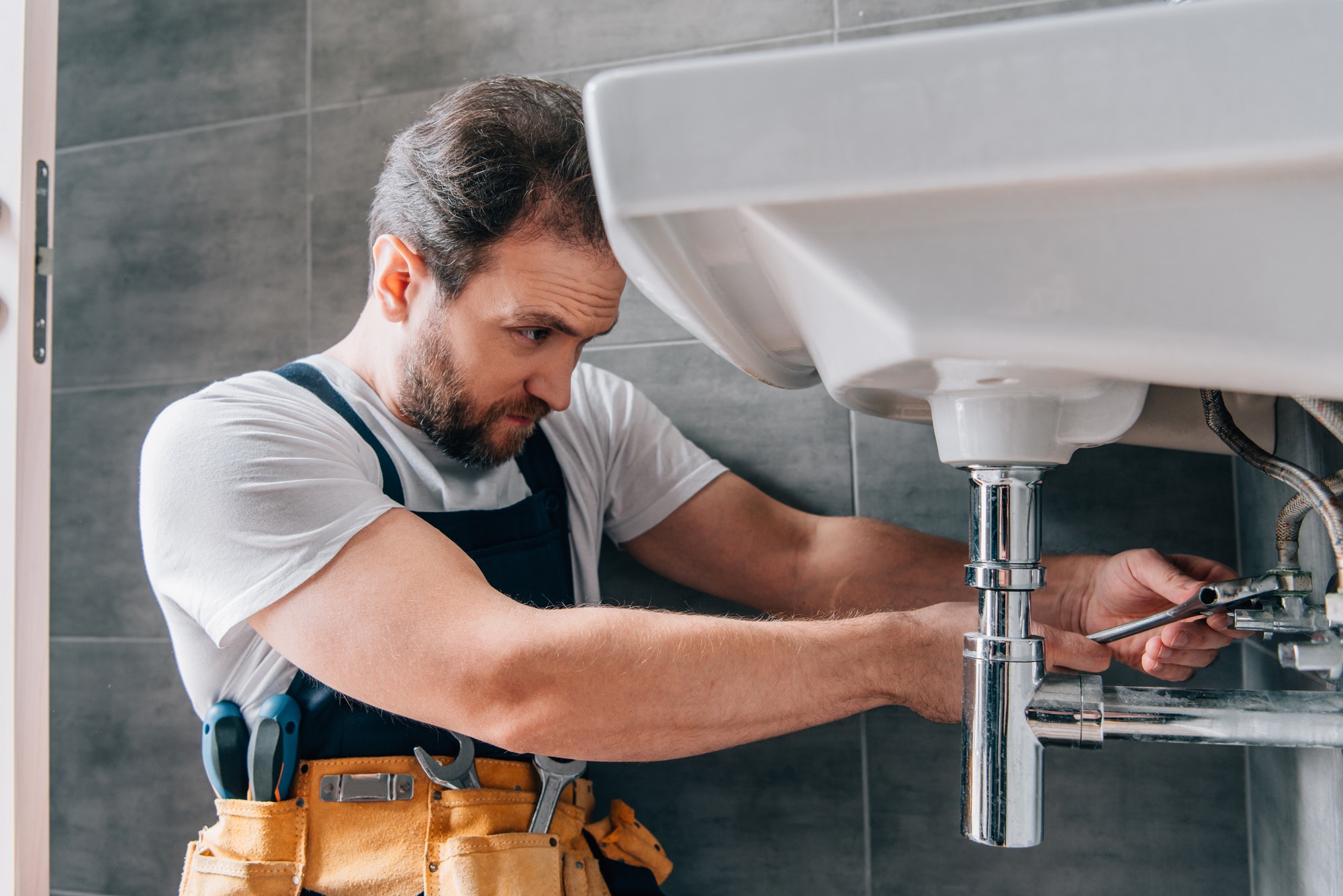 Focused male plumber in working overall fixing sink in bathroom.jpg